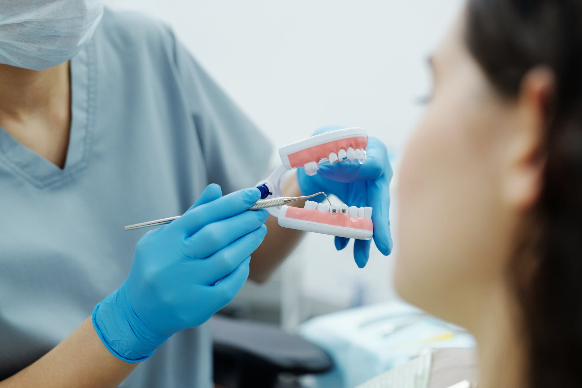 person in blue gloves showing a teeth model to a patient